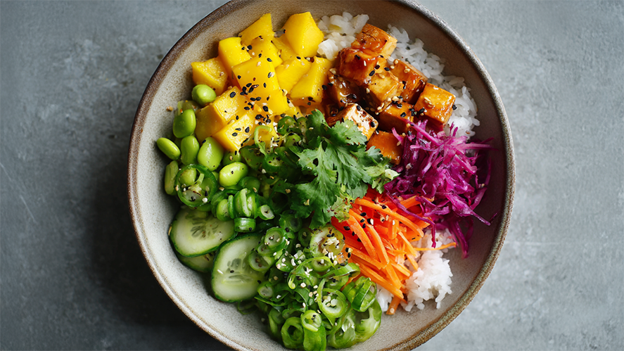 Frische Poke Bowl mit mariniertem Tofu, Mango, Edamame und lila Kohl auf weißem Reis – Draufsicht.