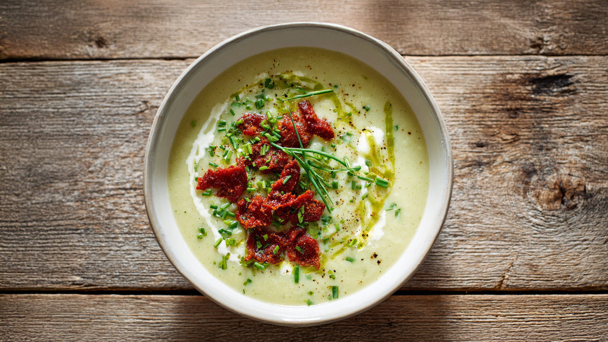 Porree-Suppe mit knusprigen Mettwurstchips und frischem Schnittlauch – cremige Wintersuppe auf rustikalem Holztisch serviert.