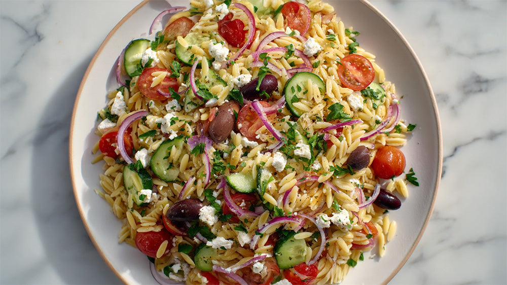 Draufsicht auf einen Teller Risoni-Salat mit Tomaten, Gurken und Feta.
