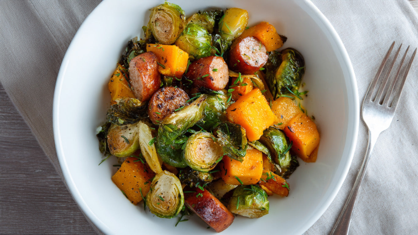Rosenkohl-Kürbis-Pfanne mit Mettenden - herzhafte Pfanne mit gebratenem Rosenkohl, Kürbiswürfeln und Wurstscheiben, serviert in einer weißen Schale.