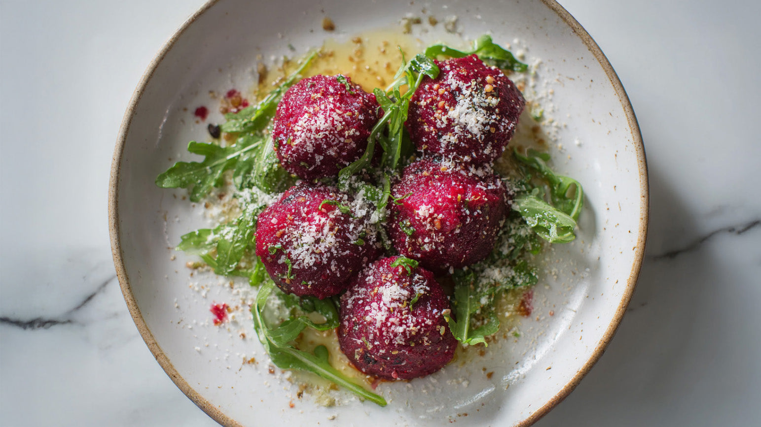 Rote Beete Knödel vegetarisch mit Rucola, Nussbutter und Parmesan in einer modernen Schüssel angerichtet.