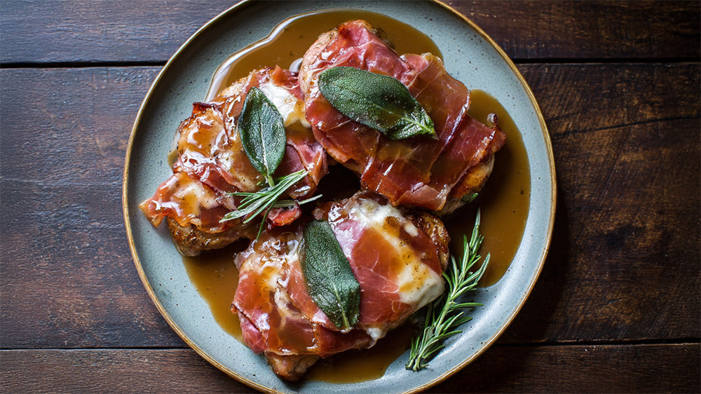 Draufsicht auf vier Saltimbocca-Steaks mit Schinken, Salbei und Sauce.