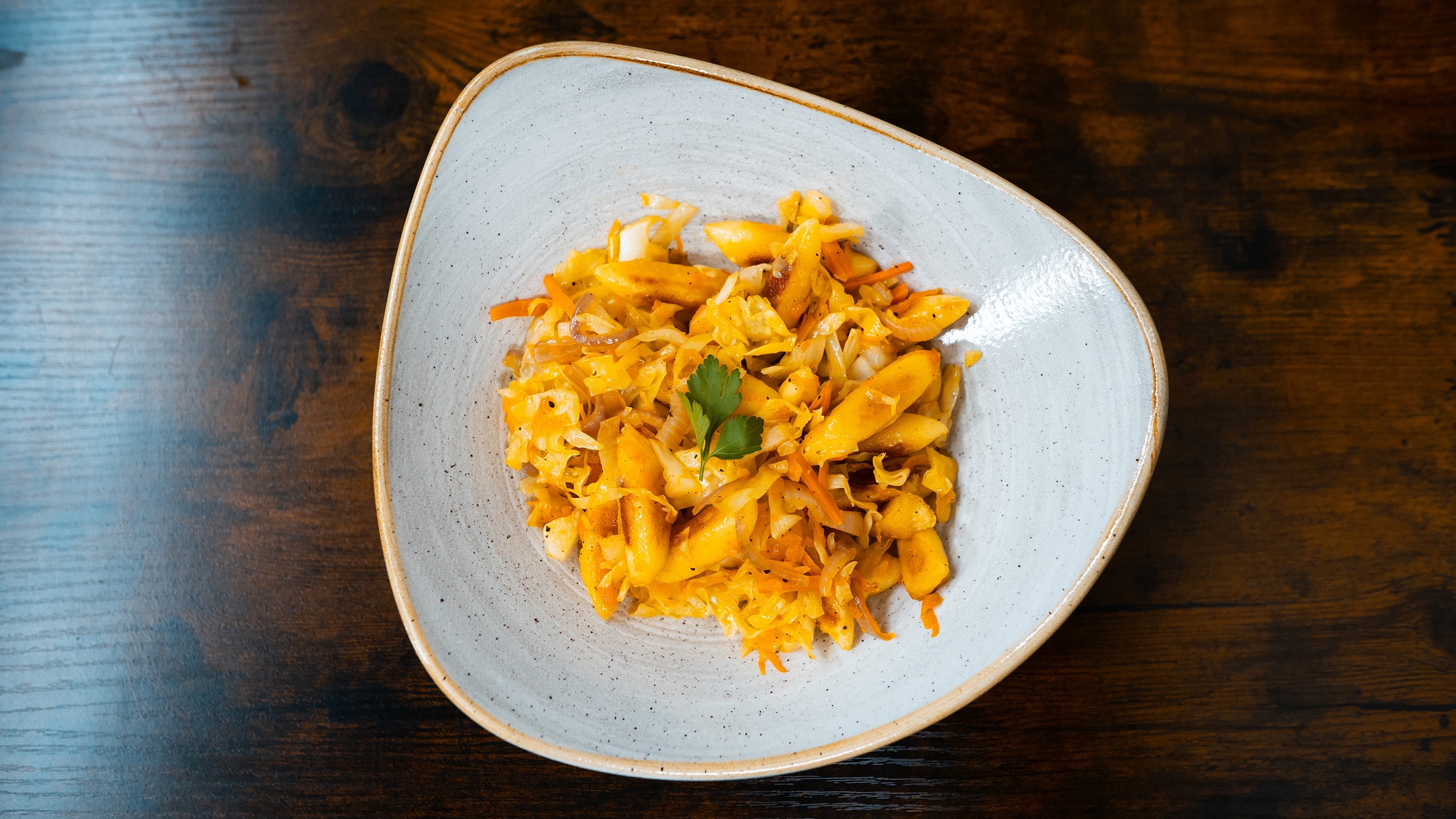 Draufsicht einer vegetarischen Schupfnudelpfanne mit Sauerkraut und Karotten, serviert in einer hellen Keramikschale auf dunklem Echtholz.