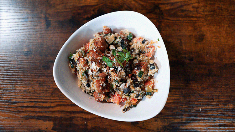 Sommer Couscous mit Zucchini, Aubergine, Tomaten, gebratener Wurst und gehackten Mandeln in einer weißen Schale von oben