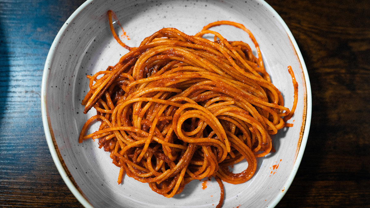 Spaghetti in dunkler Tomatensauce serviert in einer rustikalen Keramikschale auf einem dunklen Holztisch.