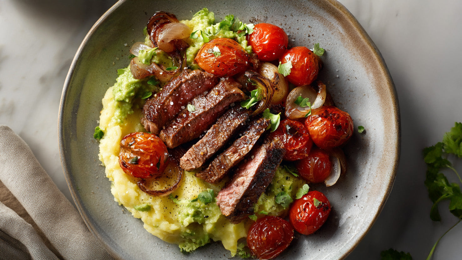 Steak-Pfanne mit Avocado-Kartoffelpüree, angerichtetes Rinderfilet in Streifen mit gebratenen Kirschtomaten und Zwiebeln auf cremigem Kartoffel-Avocado-Püree.