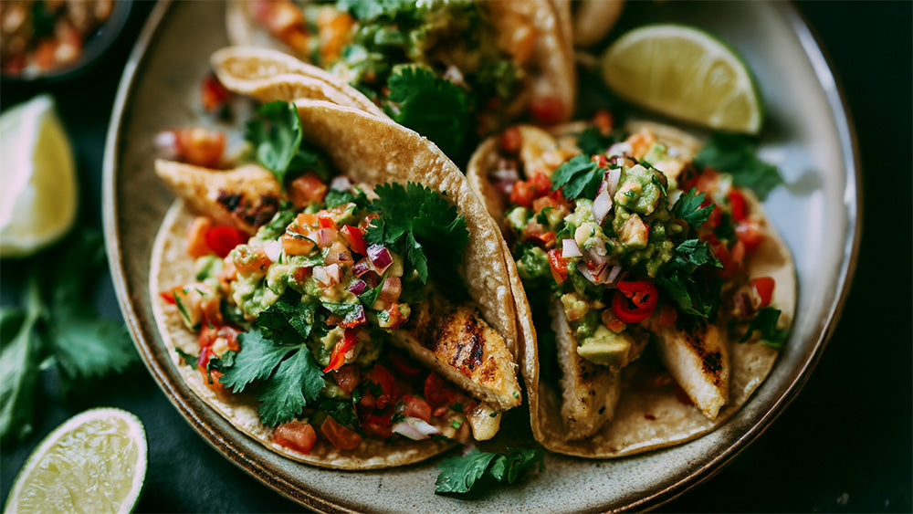 Draufsicht auf drei Maistacos mit Hähnchen, Guacamole und Salsa.