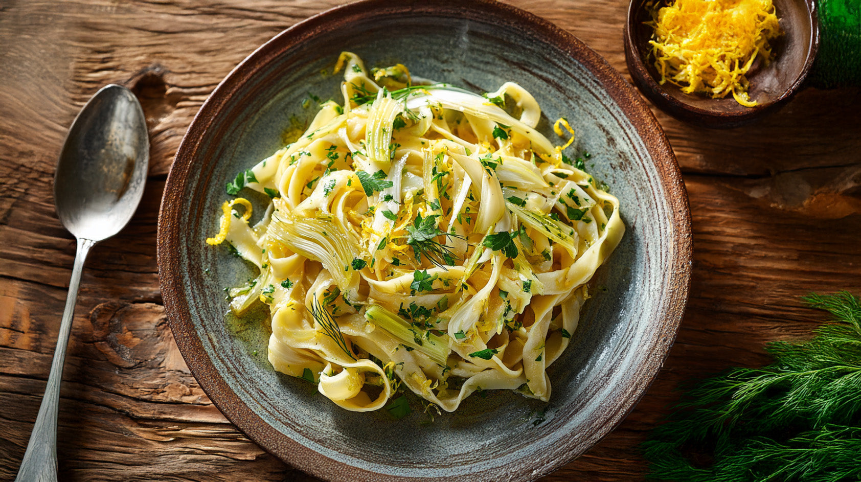 Tagliatelle mit Fenchel – frische Pasta mit Zitrone und Petersilie auf rustikalem Holztisch, leichtes mediterranes Nudelgericht.