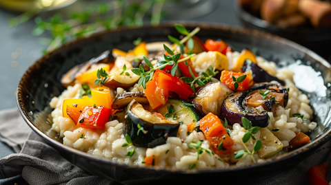 Cremiges Risotto mit Pilzen und buntem Gemüse, bestreut mit Kräutern, serviert auf dunklem Teller.