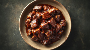 Wildgulasch in Schüssel, zart geschmorte Wildfleischwürfel in dunkler Rotweinsauce, rustikal angerichtet auf dunklem Hintergrund