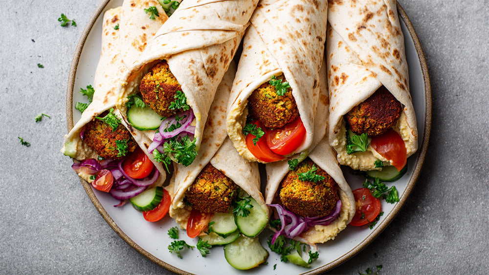 Falafel Wraps mit Hummus, Gurke, Tomaten und roten Zwiebeln auf Teller angerichtet