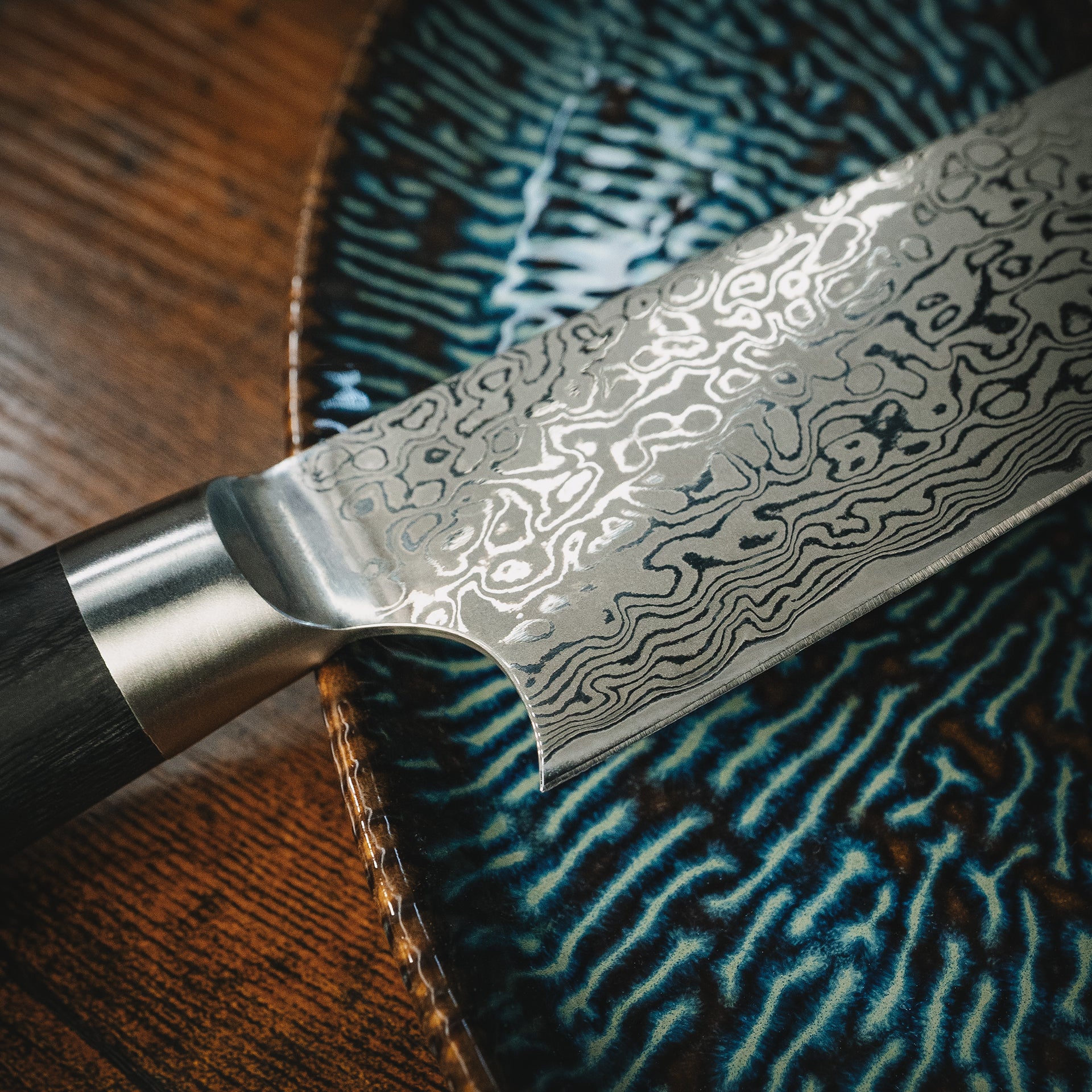 Nahaufnahme der Damastklinge des Yuno Messers auf einem Keramikteller.