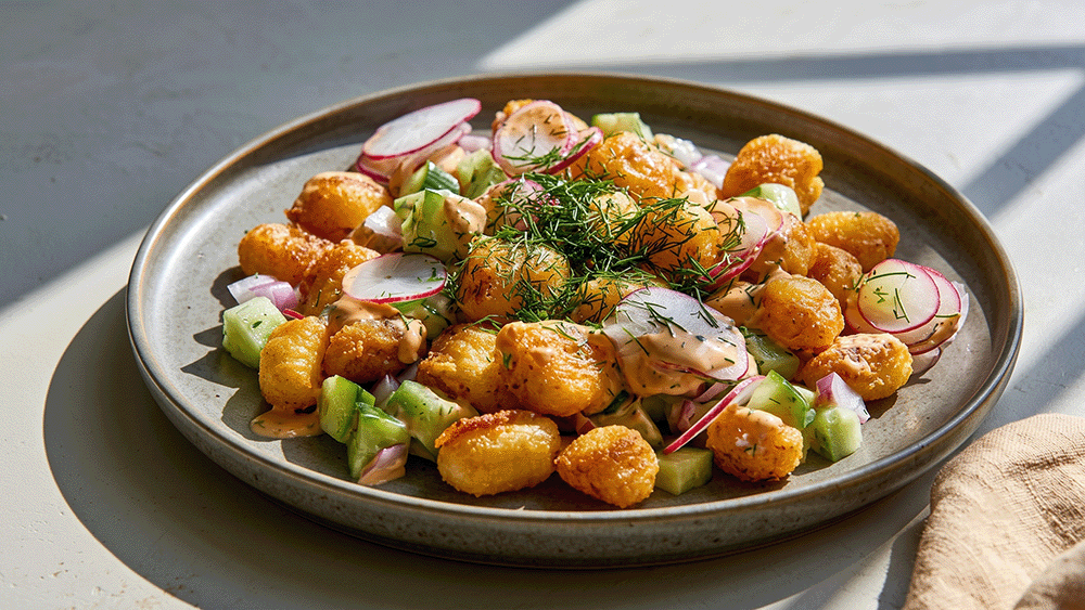 Crispy Gnocchi Salat schräg angerichtet auf einem Teller, knusprige Gnocchi mit frischem Gemüse, Radieschenscheiben und Dill, daneben ein Leinentuch.