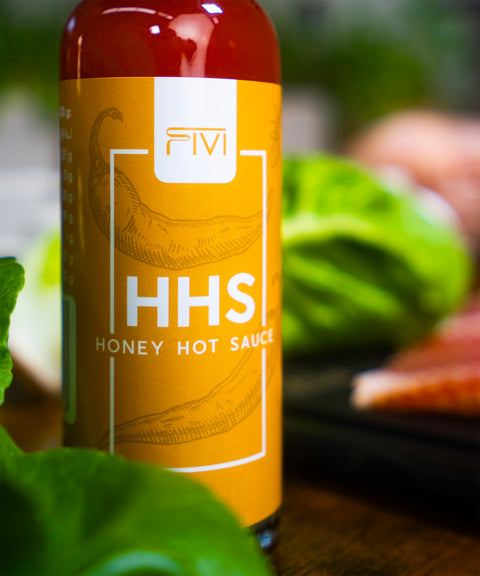 Honey Hot Sauce von FIVI – Flasche mit scharfer Sauce und Honignote vor einem Holzbrett und frischem Salat.