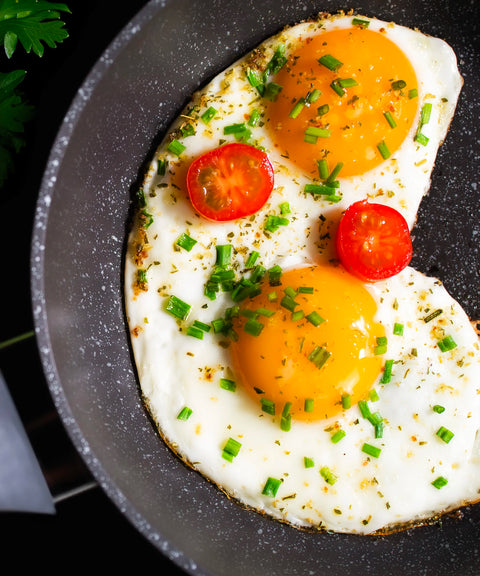 Bratpfanne von FIVI in welcher gerade zwei Spiegeleier gebraten werden mit frischen Tomaten und Schnittlauch