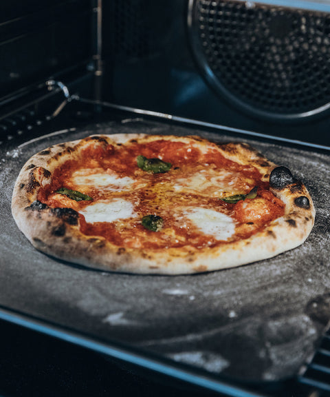 "Pizzaschieber Blacksteel von FIVI Moesta in Aktion, beim Einschieben einer Pizza in den Ofen, hitzebeständig und stabil.