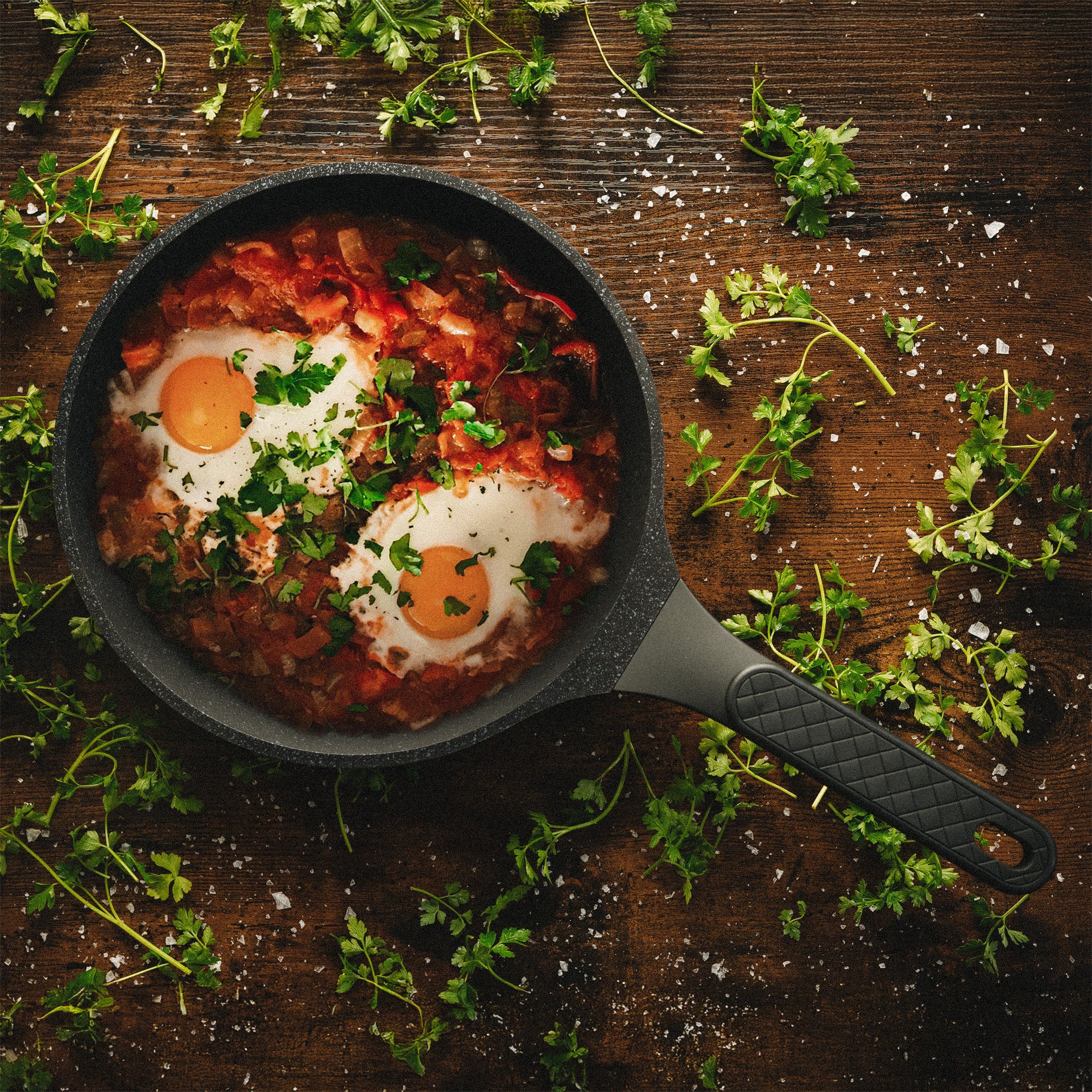 Shakshuka mit zwei Eiern direkt in der Alice Pfanne serviert auf einem Holztisch mit Petersilie.