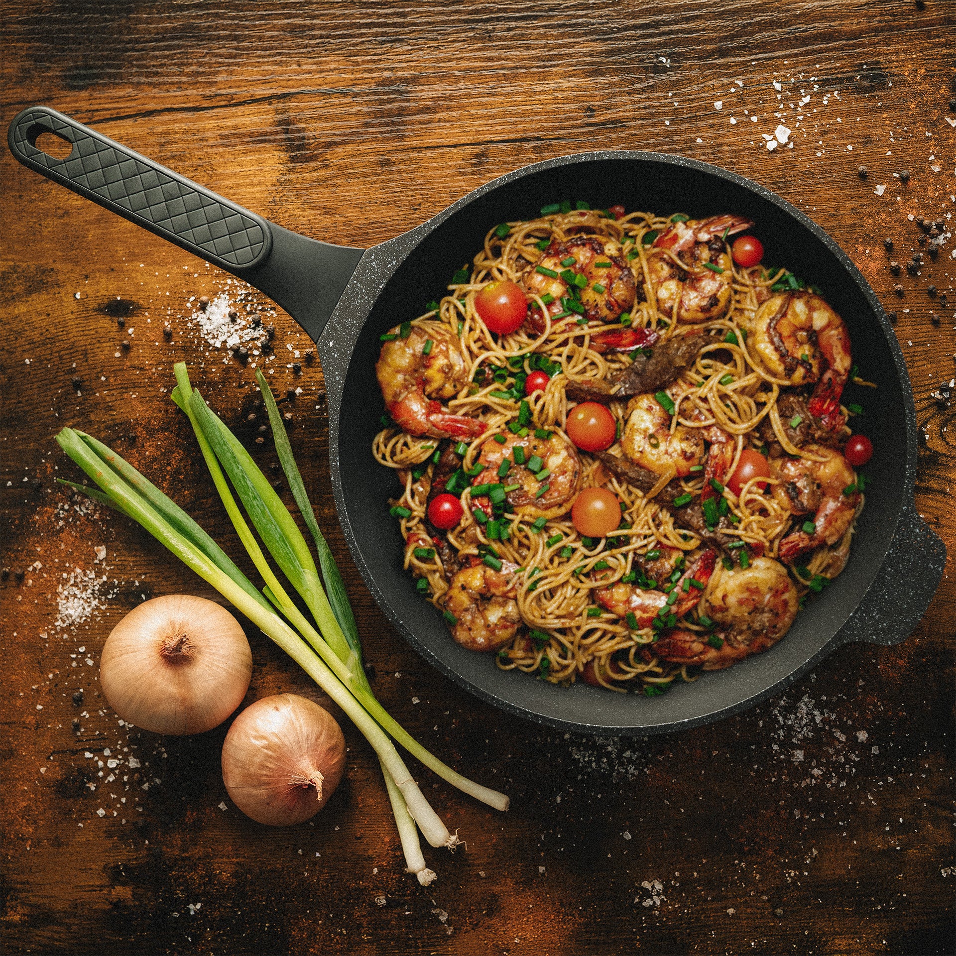 Schmorpfanne mit Pasta, Garnelen und Tomaten auf rustikalem Holztisch zur Veranschaulichung der Hitzeverteilung beim Braten.