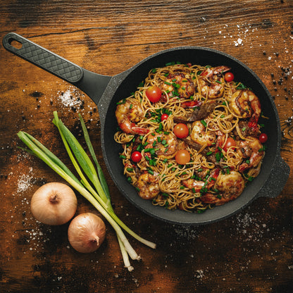 Schmorpfanne mit Pasta, Garnelen und Tomaten auf rustikalem Holztisch zur Veranschaulichung der Hitzeverteilung beim Braten.