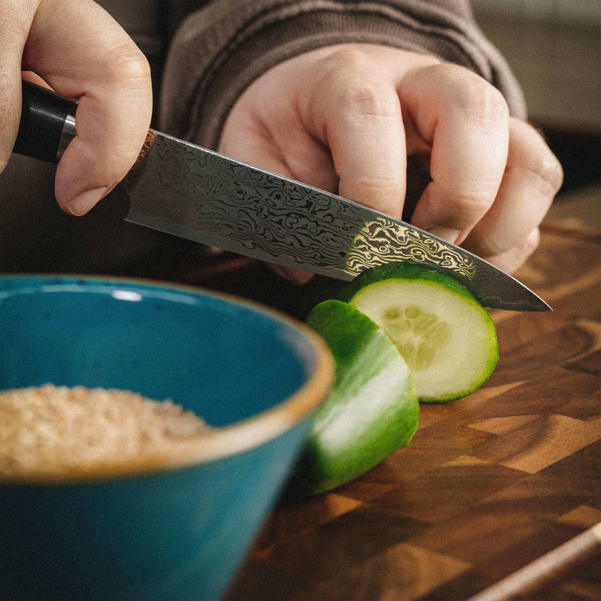 Präzises Schneiden einer Gurke mit dem scharfen Sanji Damastmesser auf einem Holzschneidebrett.