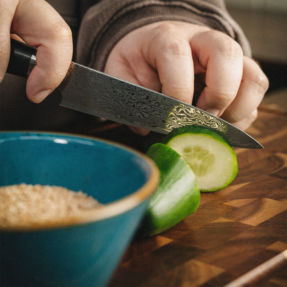 Präzises Schneiden einer Gurke mit dem scharfen Sanji Damastmesser auf einem Holzschneidebrett.