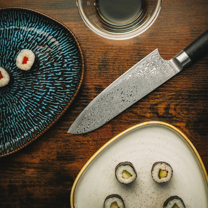 Ästhetisches Küchen-Arrangement mit dem Akira Santokumesser, Sushi und Sojasauce auf dunklem Echtholz.
