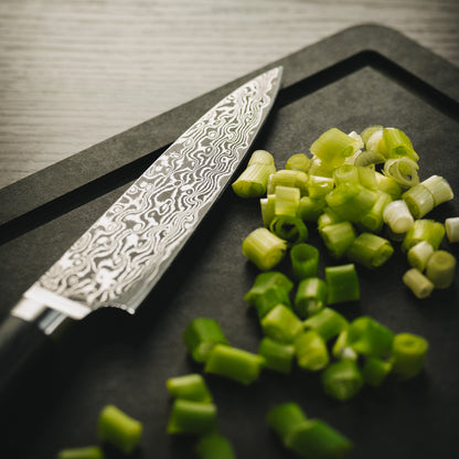 Nahaufnahme des Sanji Pettymessers neben fein gehackten Frühlingszwiebeln auf einem dunklen Brett.