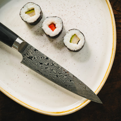 Draufsicht auf die Damastklinge des Sanji Pettymessers neben handgerollten Sushi-Stücken.