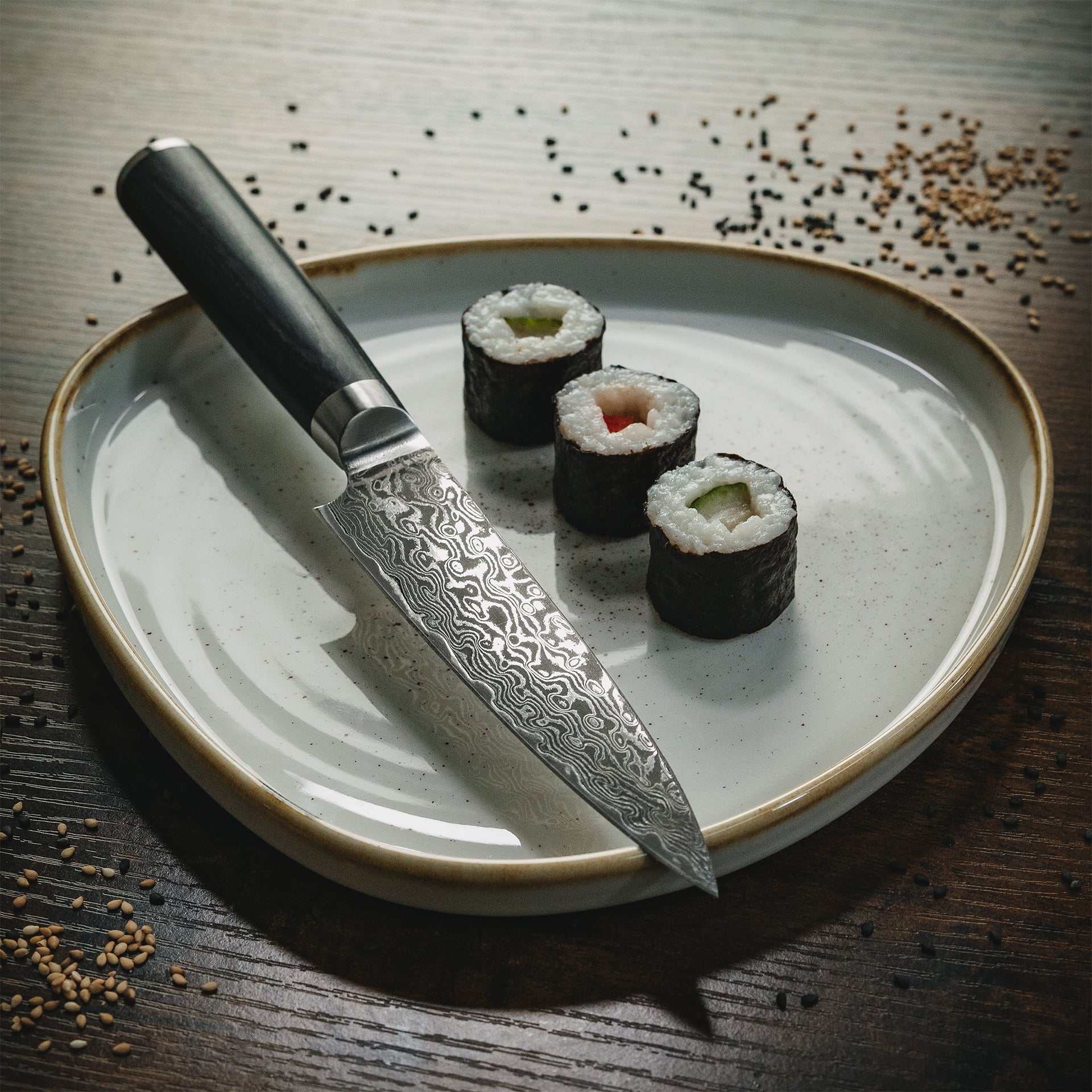 Ästhetisches Stillleben: Sanji Messer auf einem Keramikteller mit Maki-Sushi und schwarzem Sesam.