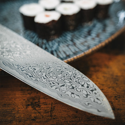 Detailansicht der Messerspitze des Akira Santokumessers vor einer Platte mit Maki-Sushi.