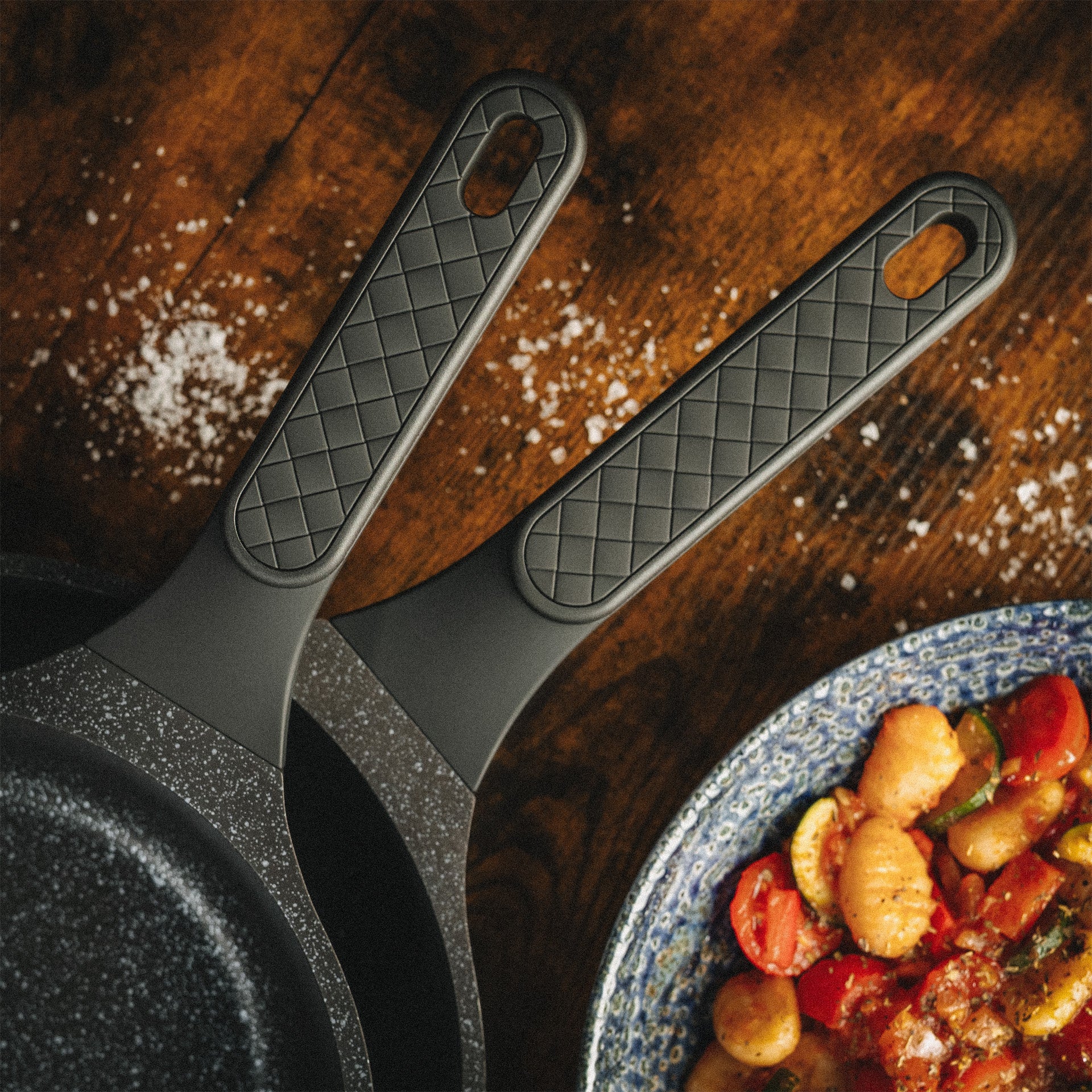 Nahaufnahme der ergonomischen Griffe der Pfannen Alice und Utz neben einem mediterranen Gnocchi-Gericht.