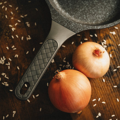 Detailansicht des ergonomischen Griffs der Utz Pfanne mit Rautenmuster neben frischen Zwiebeln.