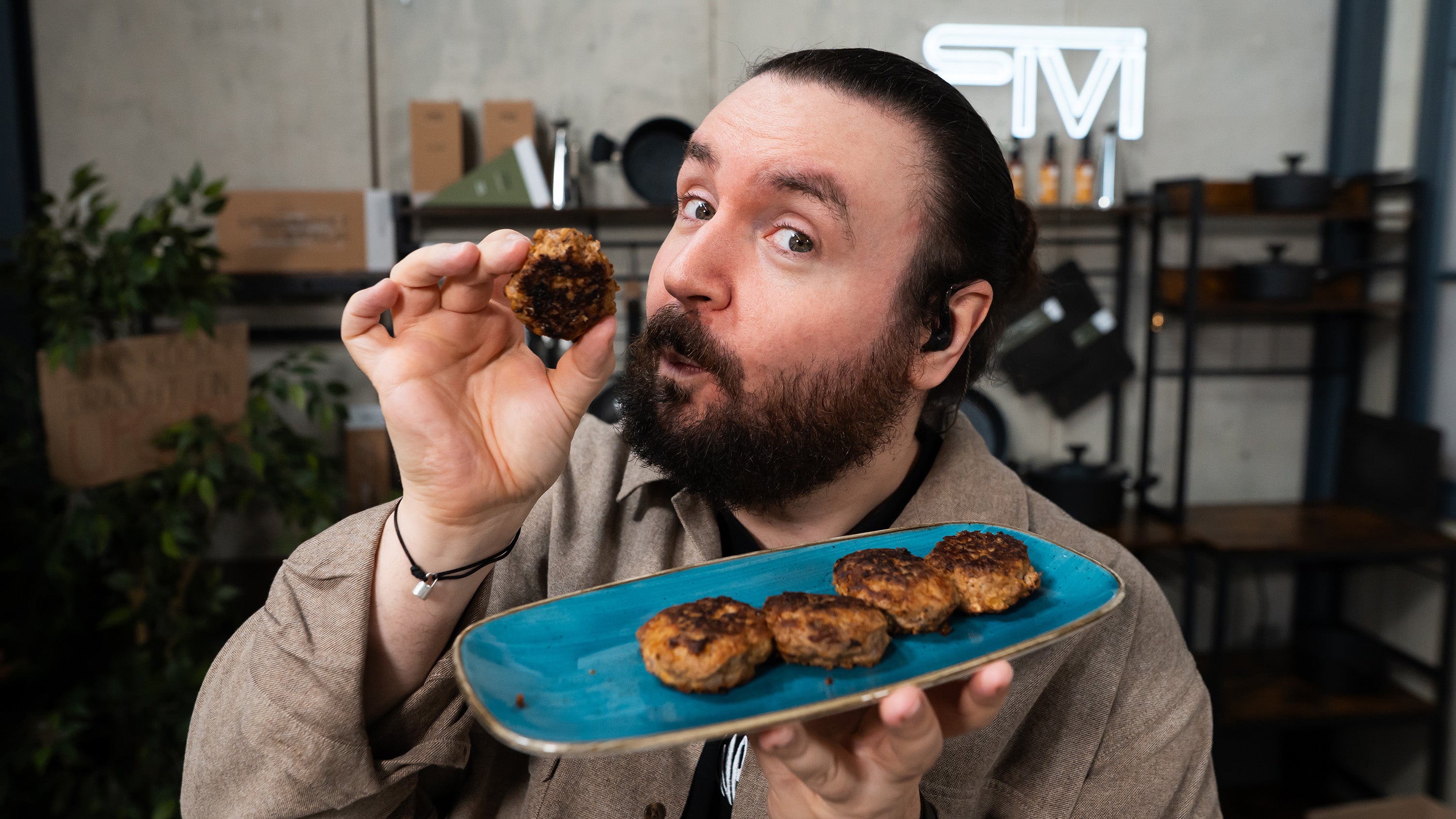 Sturmwaffel hält eine selbstgemachte Frikadelle in der Hand und präsentiert einen blauen Teller mit Fleischpflanzerln in einer fivi-Küche.