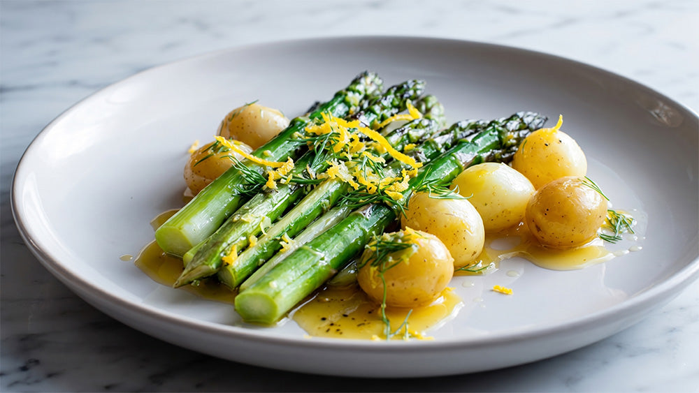 Seitenansicht von angerichtetem grünen Spargel und goldgelben Kartoffeln in Zitronenbutter, serviert auf einem hellen Teller vor Marmorhintergrund.