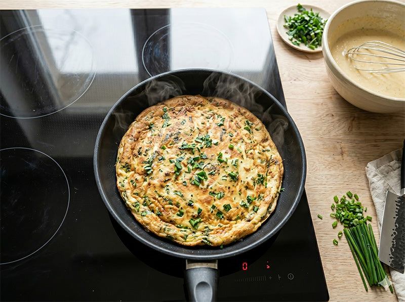 Kräuterpfannkuchen wird in einer schwarzen Pfanne auf einem Ceranfeld goldbraun gebacken.