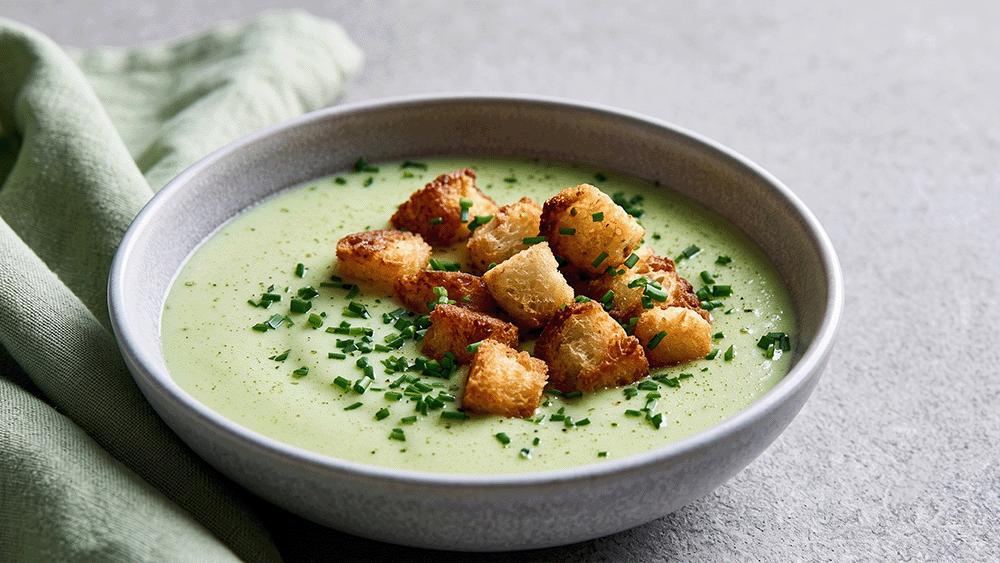Cremige Melonen-Gurken-Suppe in grauer Schale, angerichtet mit goldbraunen Croûtons und Schnittlauchröllchen