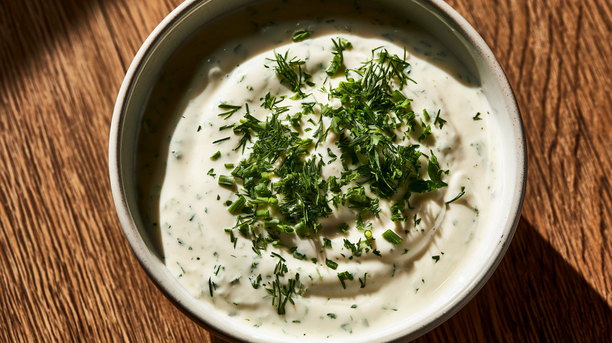 Nahaufnahme von cremigem Ranch Dressing in einer Schale, bestreut mit Dill und Schnittlauch, im warmen Licht auf einem Holztisch fotografiert