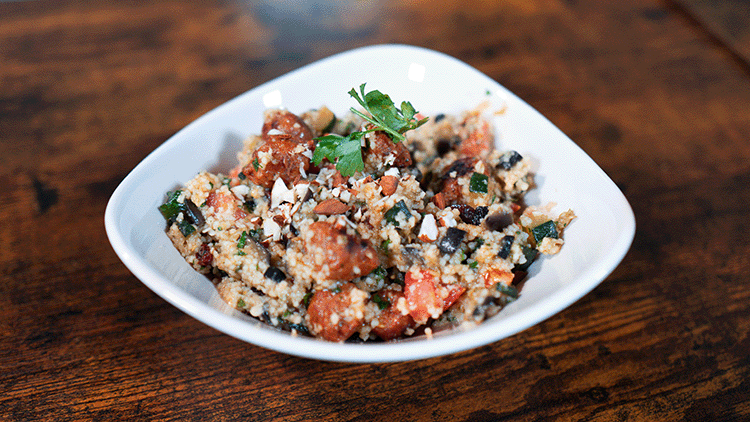 Sommer Couscous mit Gemüse, Mandeln und frischer Petersilie in einer weißen Schale auf einem rustikalen Holztisch